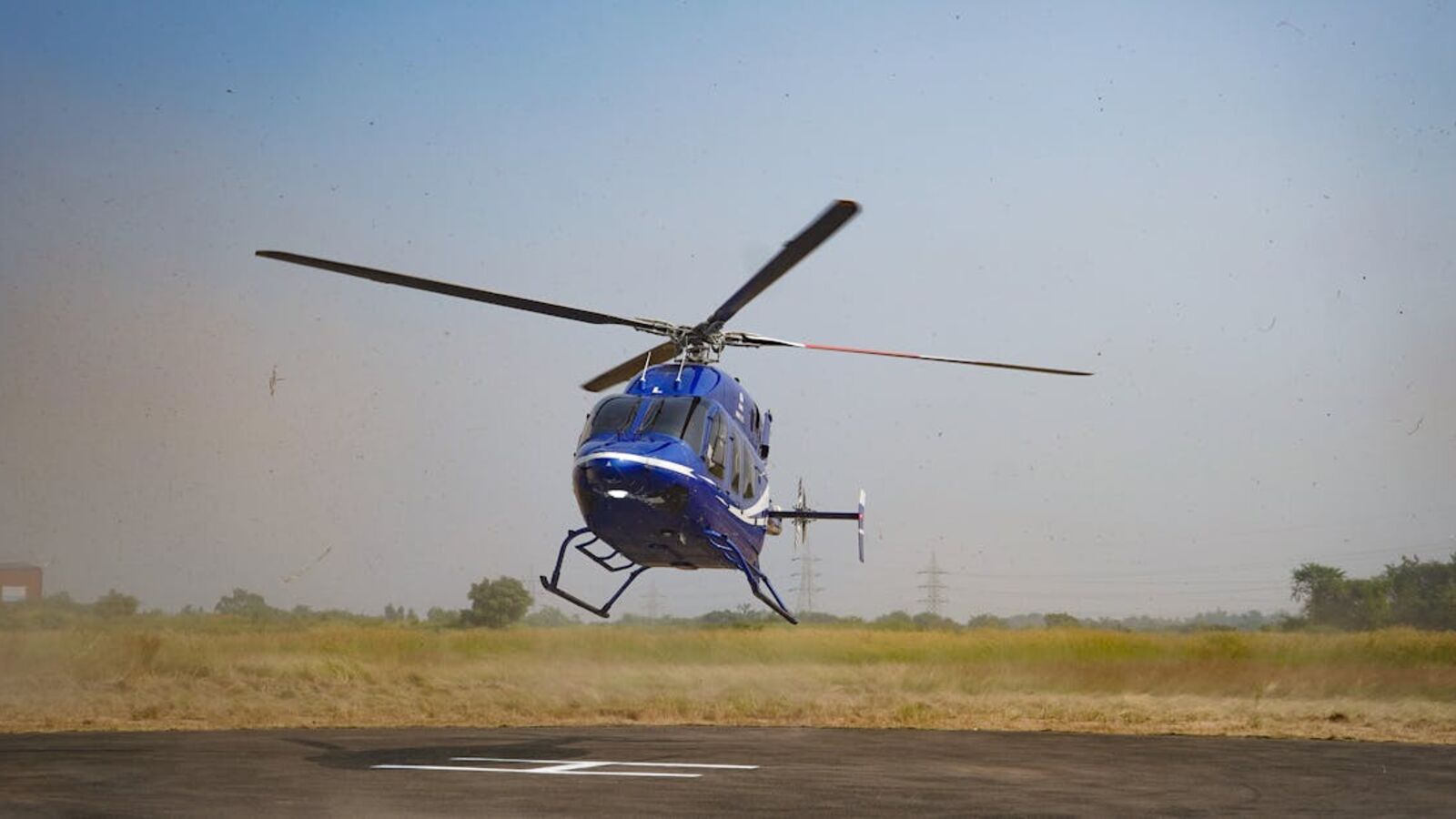 Выкуп корпоративных вертолётов в Санкт-Петербурге — A blue helicopter descends onto a helipad in a grassy outdoor setting.