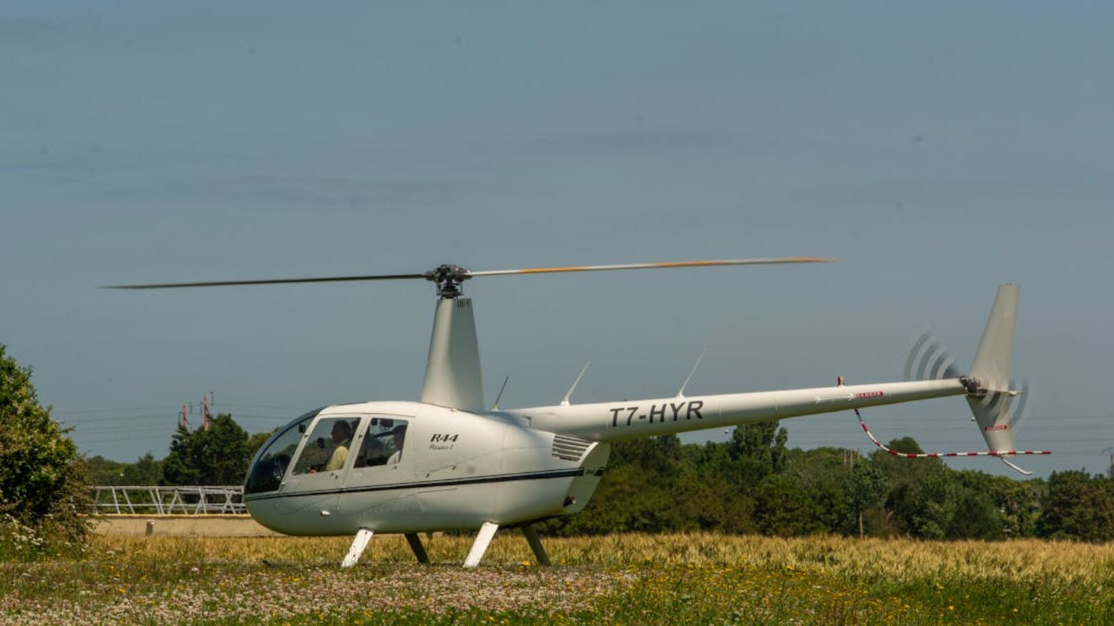 White helicopter standing on a grassy field on a sunny day with clear skies.