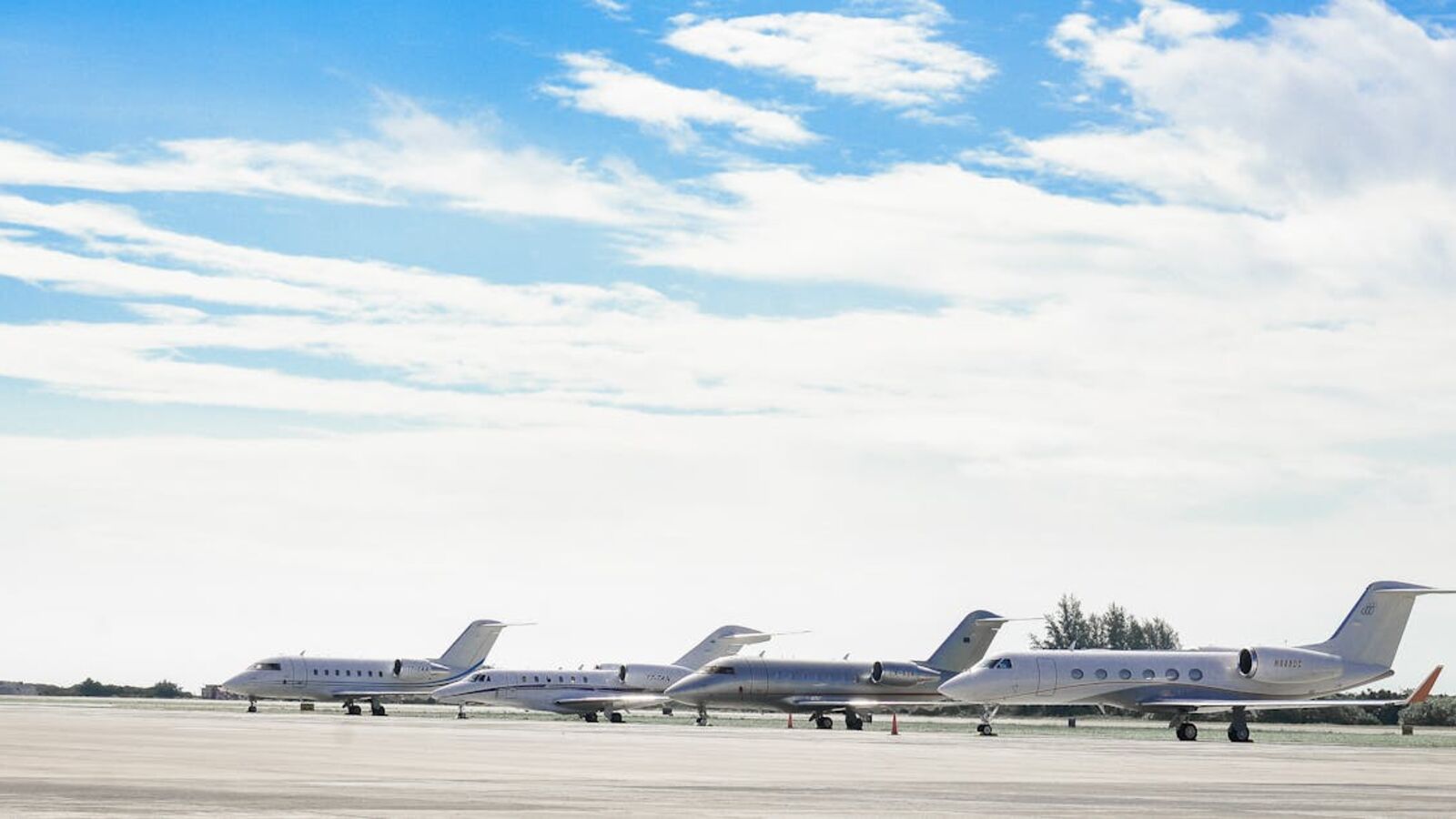Row of private jets parked on a clear day at an open runway, showcasing aviation and luxury travel.