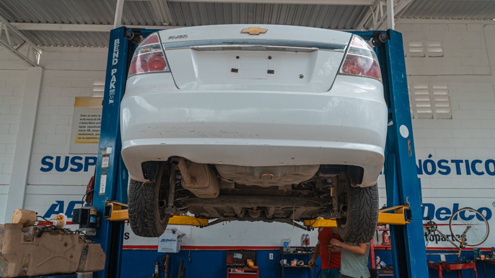 A white Chevrolet car is lifted for maintenance in an automotive repair shop.