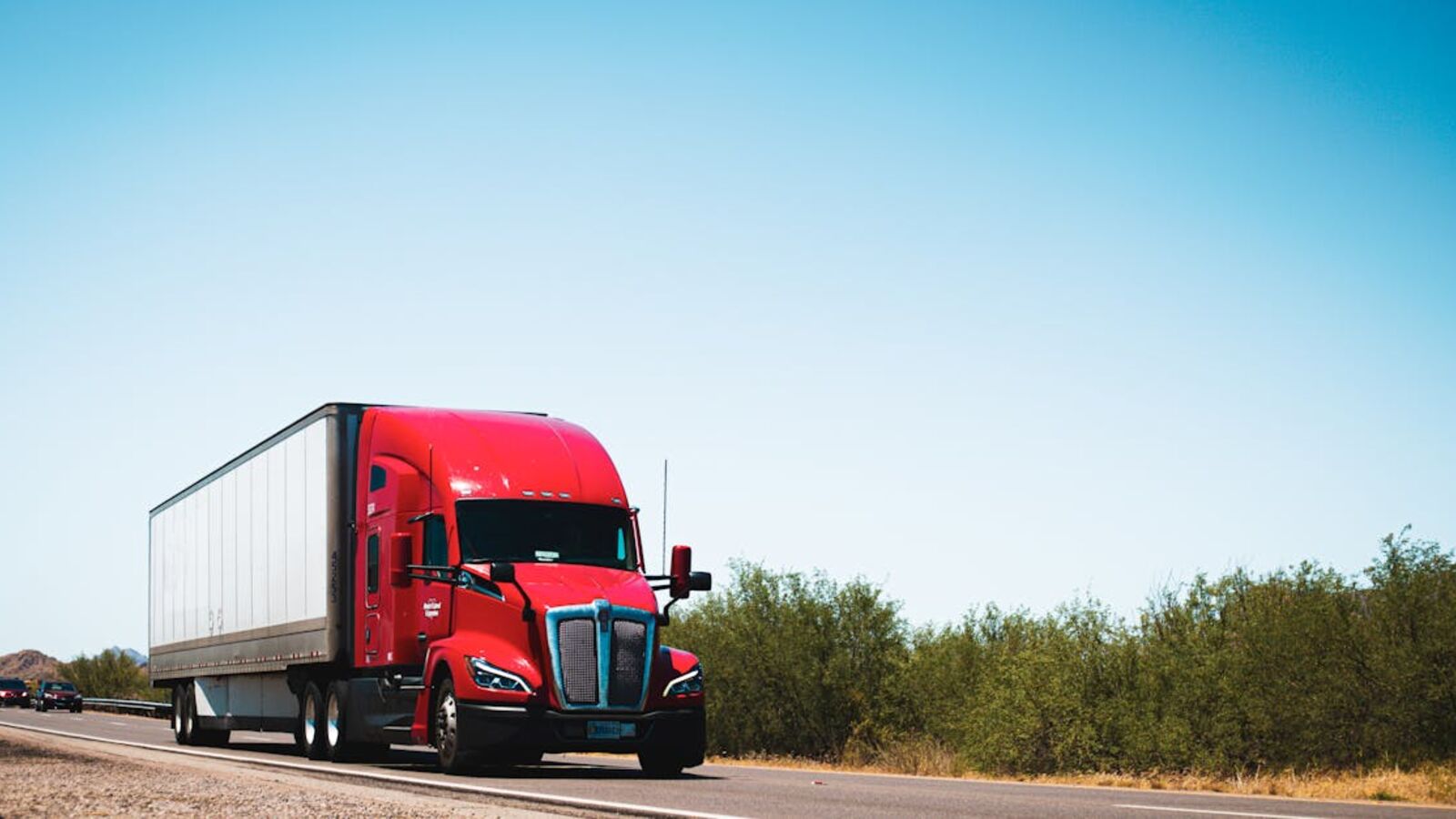 Vibrant red semi-trailer truck driving on an open highway under a clear blue sky.