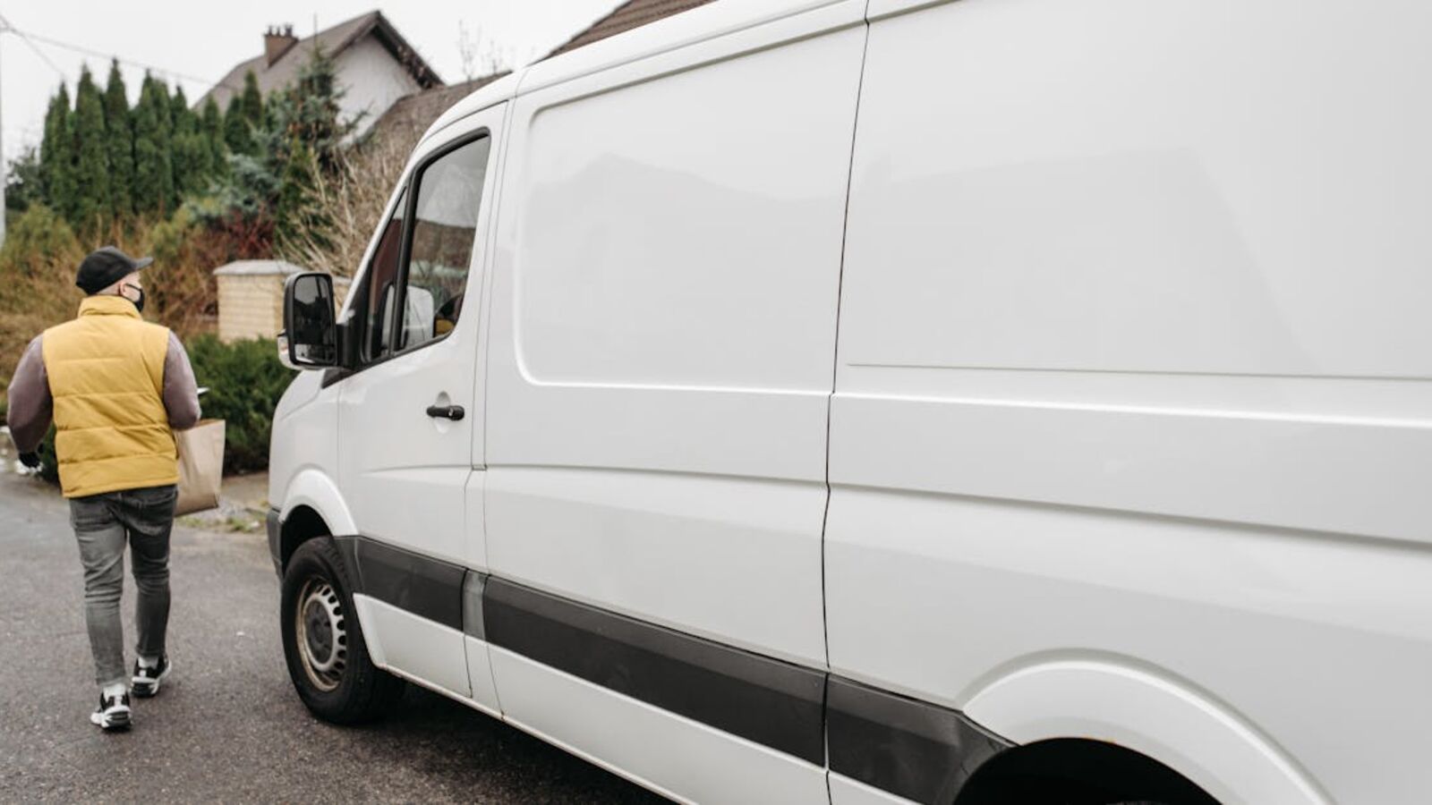 Выкуп микроавтобусов в Санкт-Петербурге — A delivery person carrying a package away from a delivery van outdoors, showcasing efficient logistics.