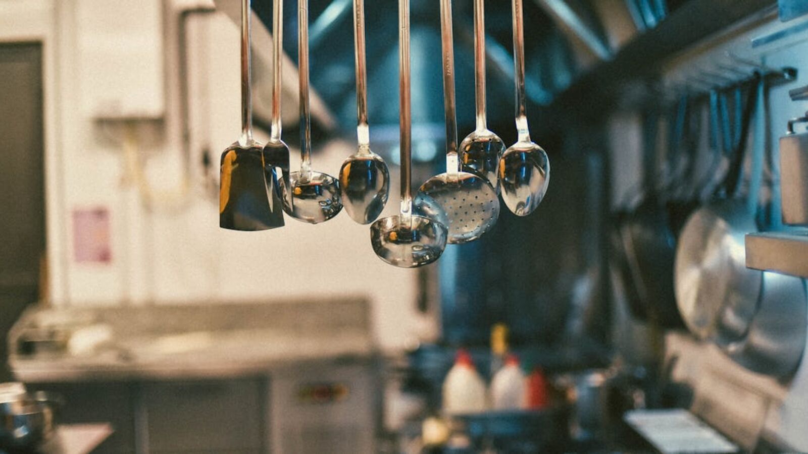 Stainless steel kitchen utensils hanging in a modern kitchen setting with blurred background.