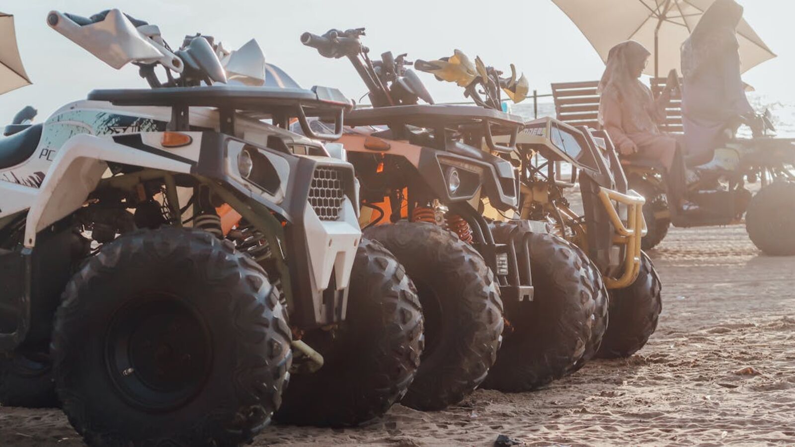 Выкуп багги в Санкт-Петербурге — ATVs lined up in the desert with riders enjoying an offroad adventure under umbrellas.