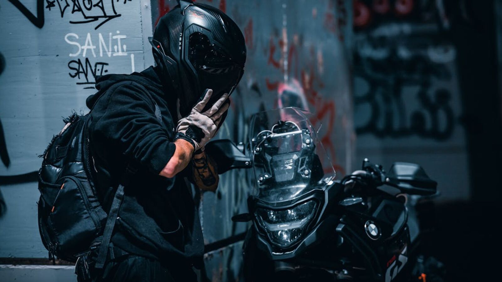 A motorcyclist poses in an urban alley setting with graffiti, creating a mysterious and edgy atmosphere.