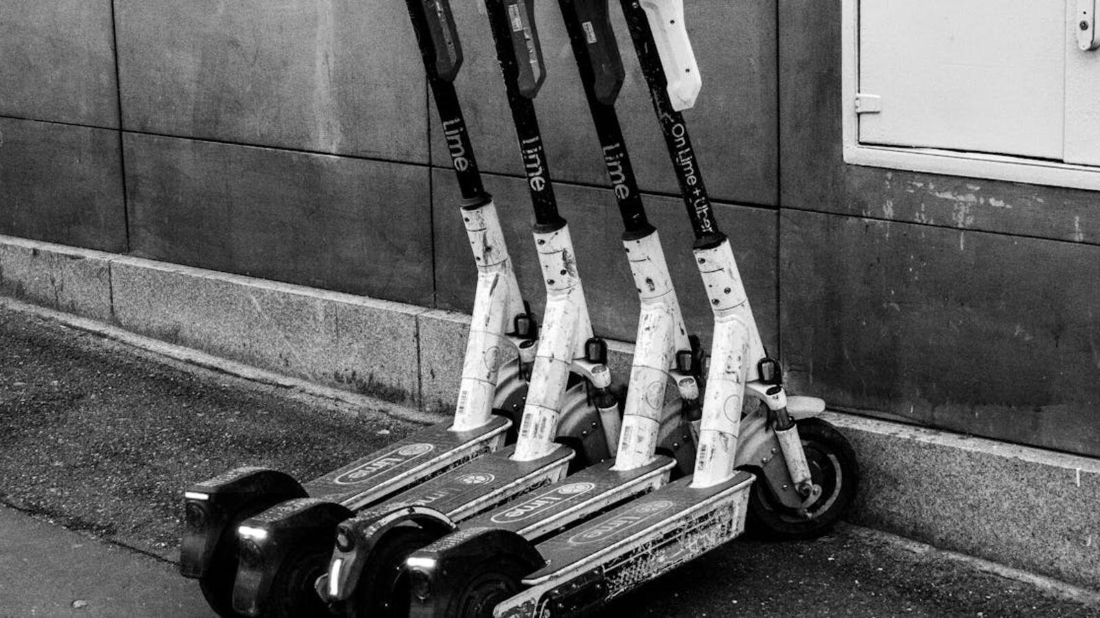 A group of electric scooters parked against a building wall, highlighting urban transportation.