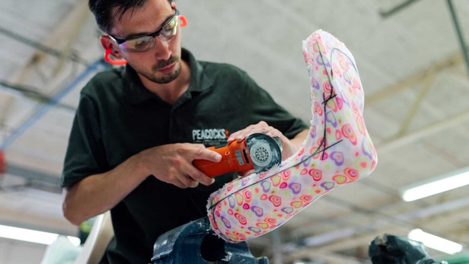 Orthotic technician using power tool to craft a colorful ankle foot orthosis in a workshop.