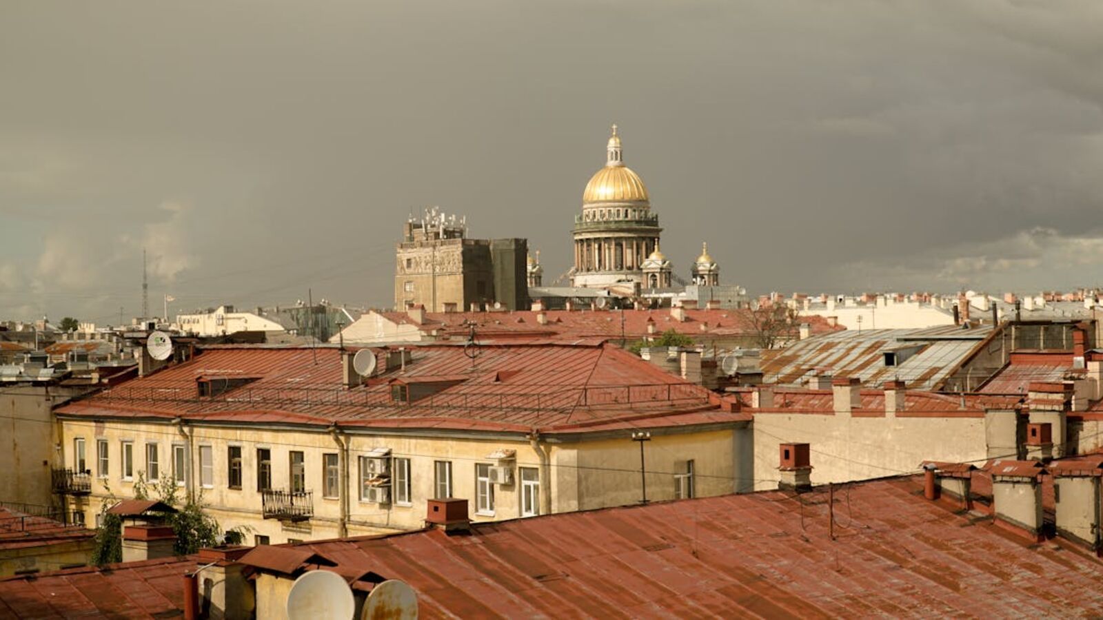 View of St. Petersburg rooftops with St. Isaac's Cathedral under a stormy sky.