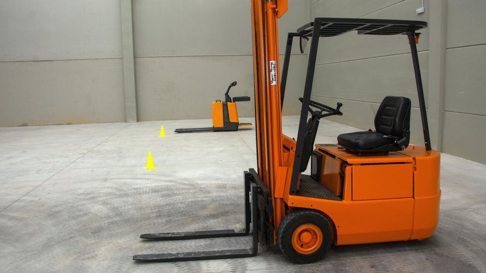 An orange forklift in a spacious warehouse with concrete floors and minimal equipment.