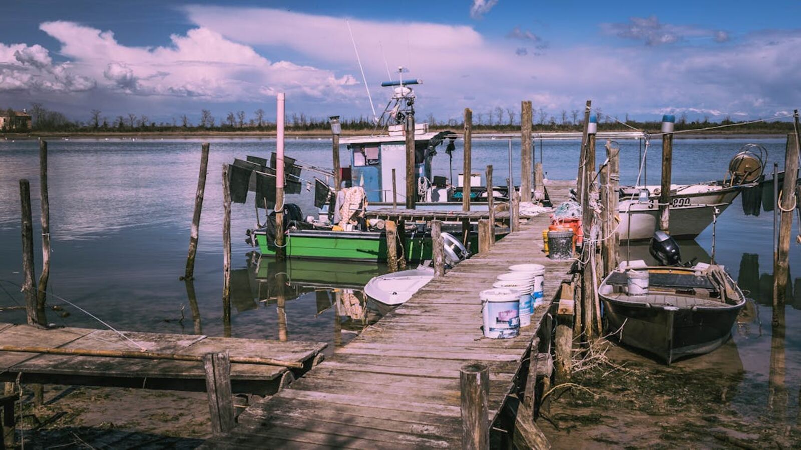 Выкуп лодок в Санкт-Петербурге — Scenic view of a weathered dock with fishing boats on a calm lake under a bright blue sky.