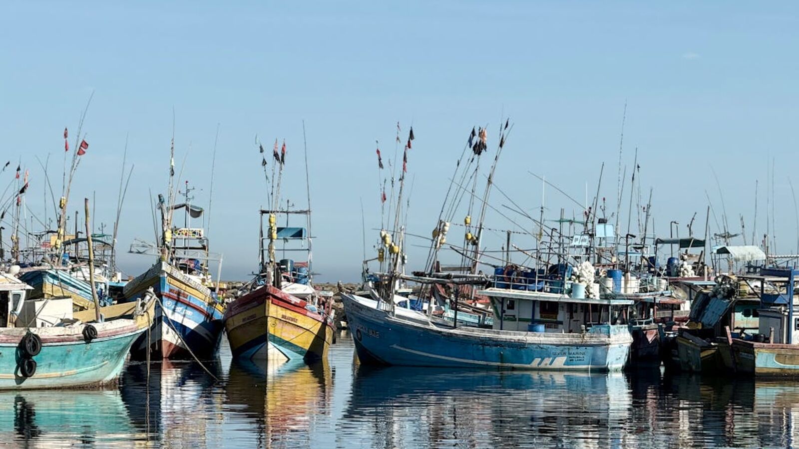 Docked fishing boats at a harbor reflecting on still waters under a blue sky.