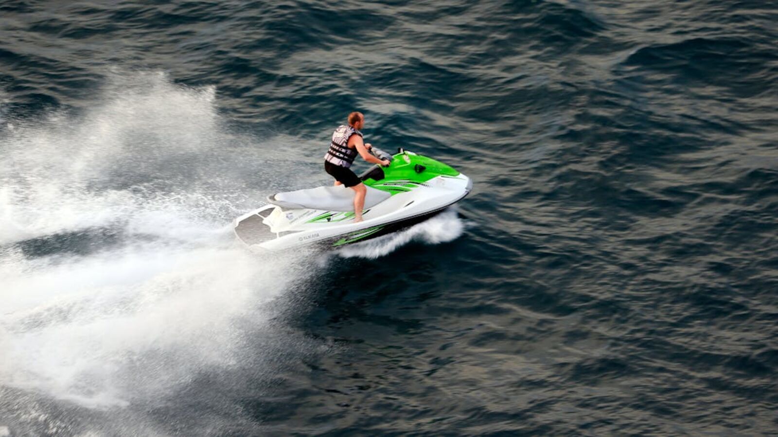 A man on a green and white jet ski speeding across the ocean on a sunny day.
