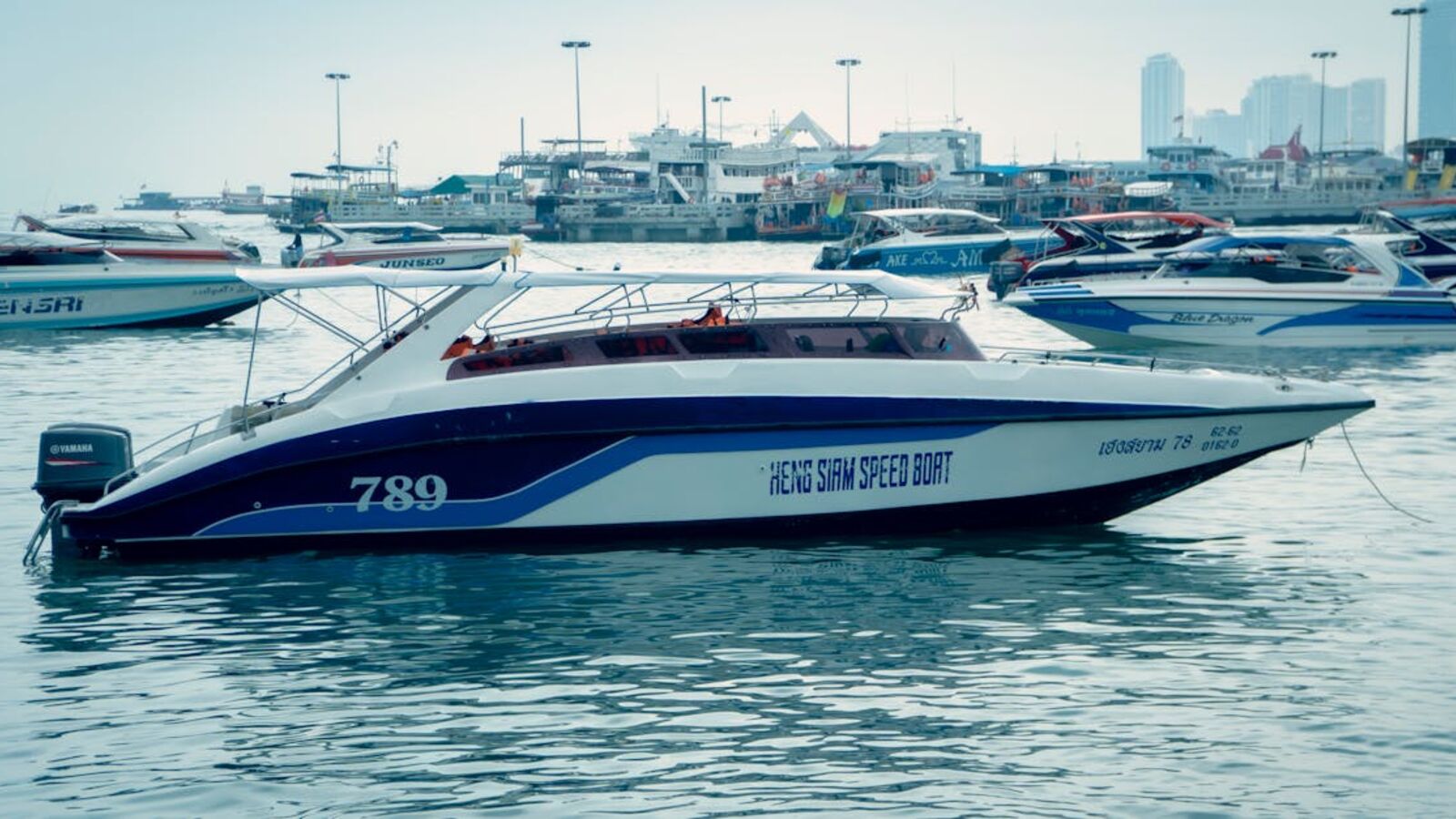 A speedboat moored in a busy marina, surrounded by other boats with a cityscape in the background.