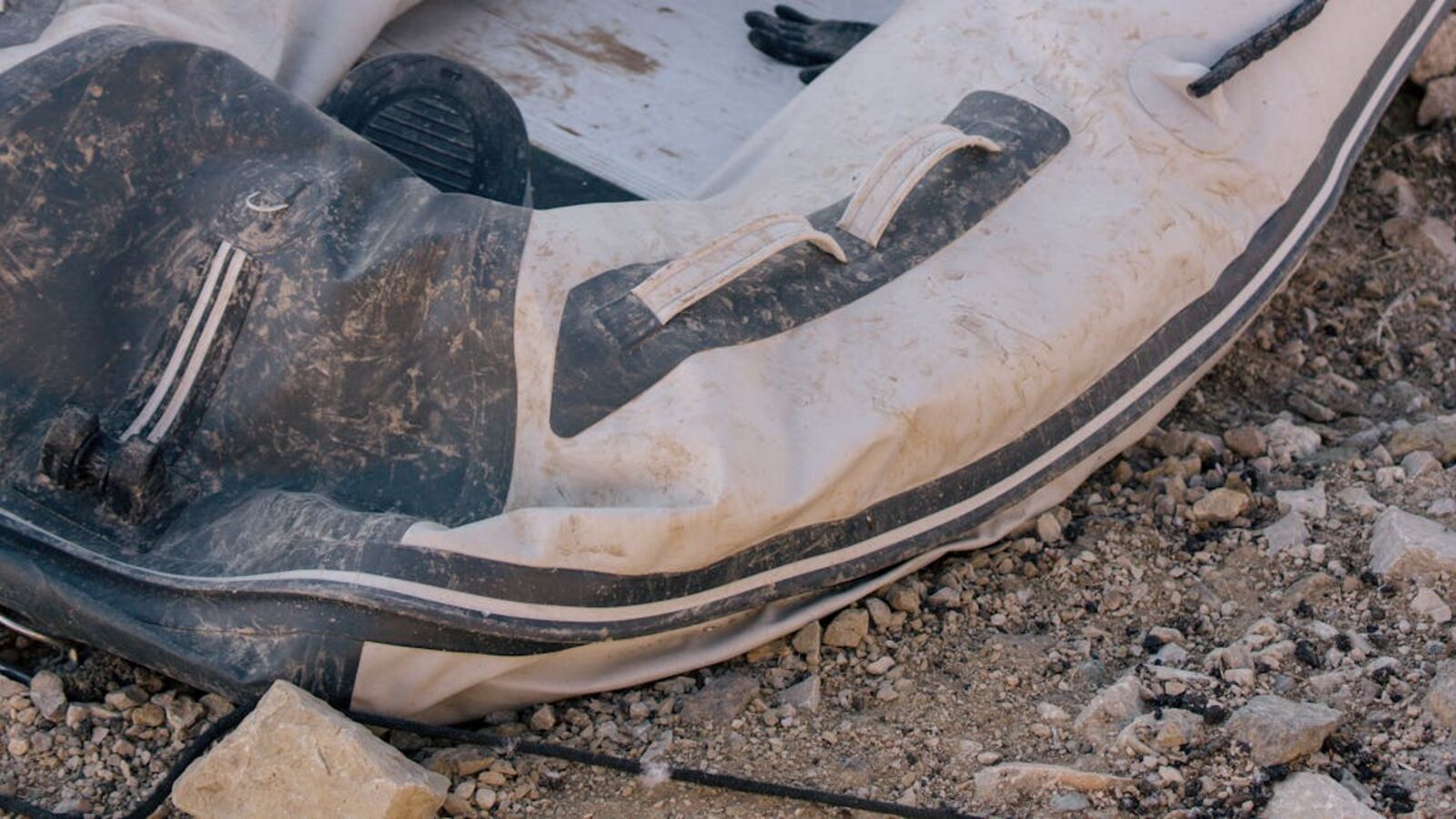 Выкуп RIB-лодок в Санкт-Петербурге — Close-up view of a weathered inflatable boat resting on a rocky beach, conveying adventure.