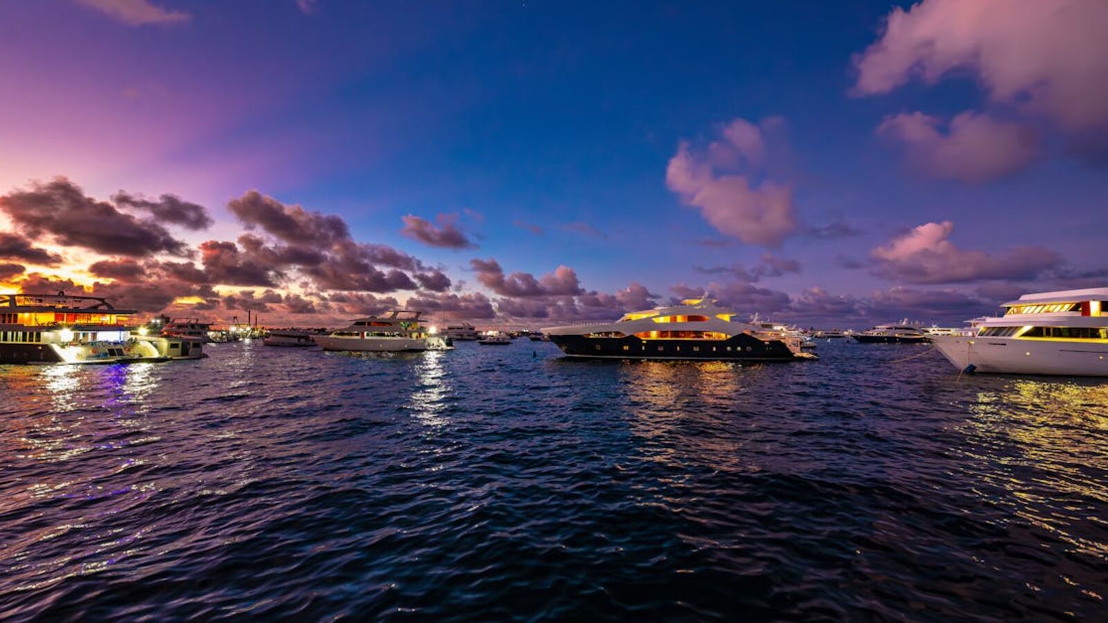A serene sunset view of luxury yachts anchored in the Maldives, reflecting vibrant colors on the water.